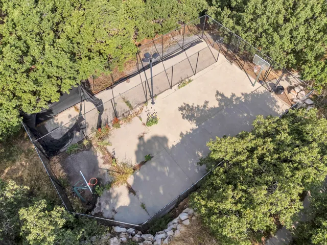 Enclosed concrete court featuring black chain-link fencing, dual basketball hoops, and integrated lighting fixtures