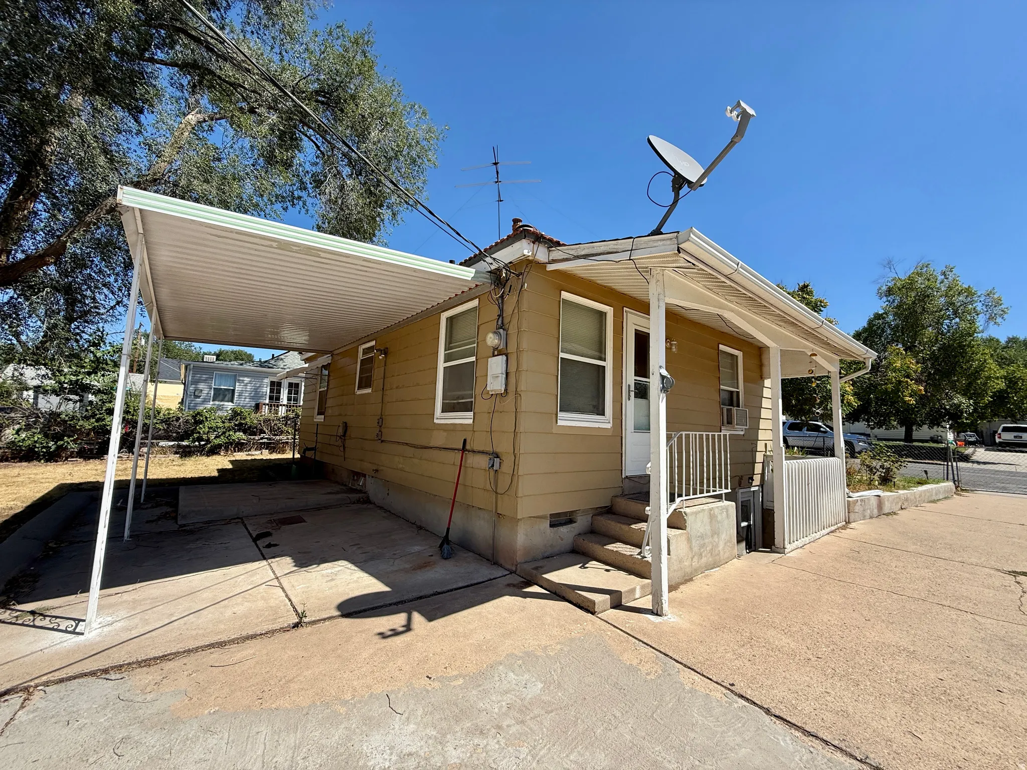 Exterior featuring tan siding, a covered carport, concrete patio, concrete steps, and a white railing