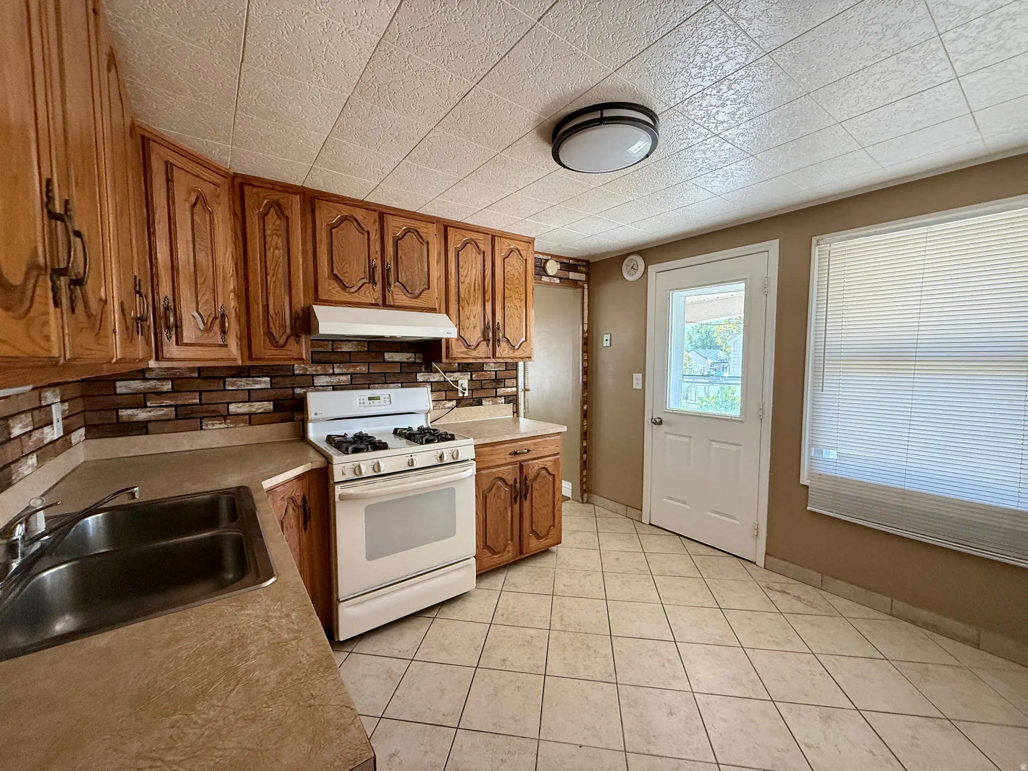 Kitchen featuring wood cabinetry, brick-patterned backsplash, a double basin stainless steel sink, and a white gas range