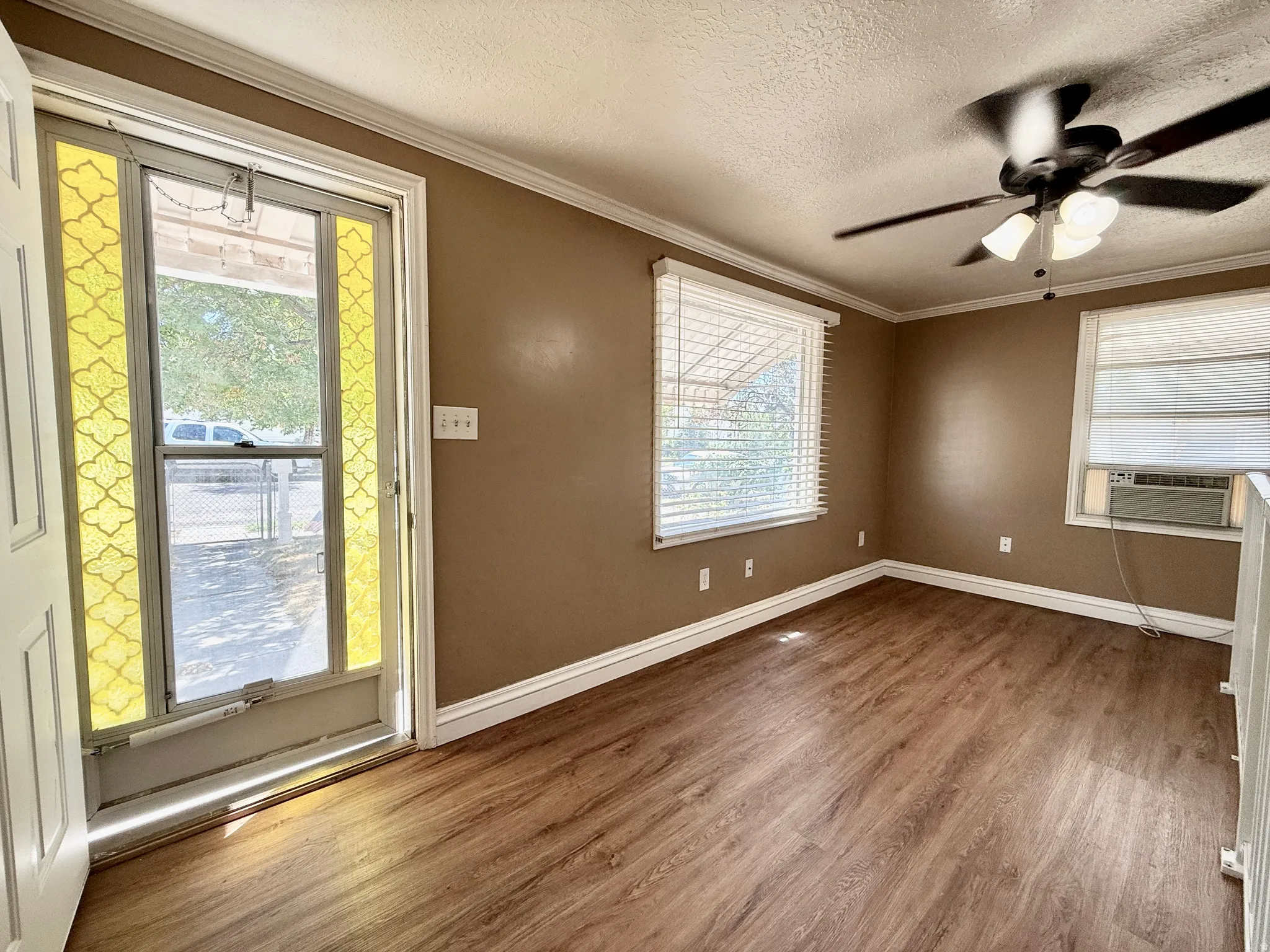 Wood-finish flooring, ceiling fan with light fixture, window blinds, and crown molding