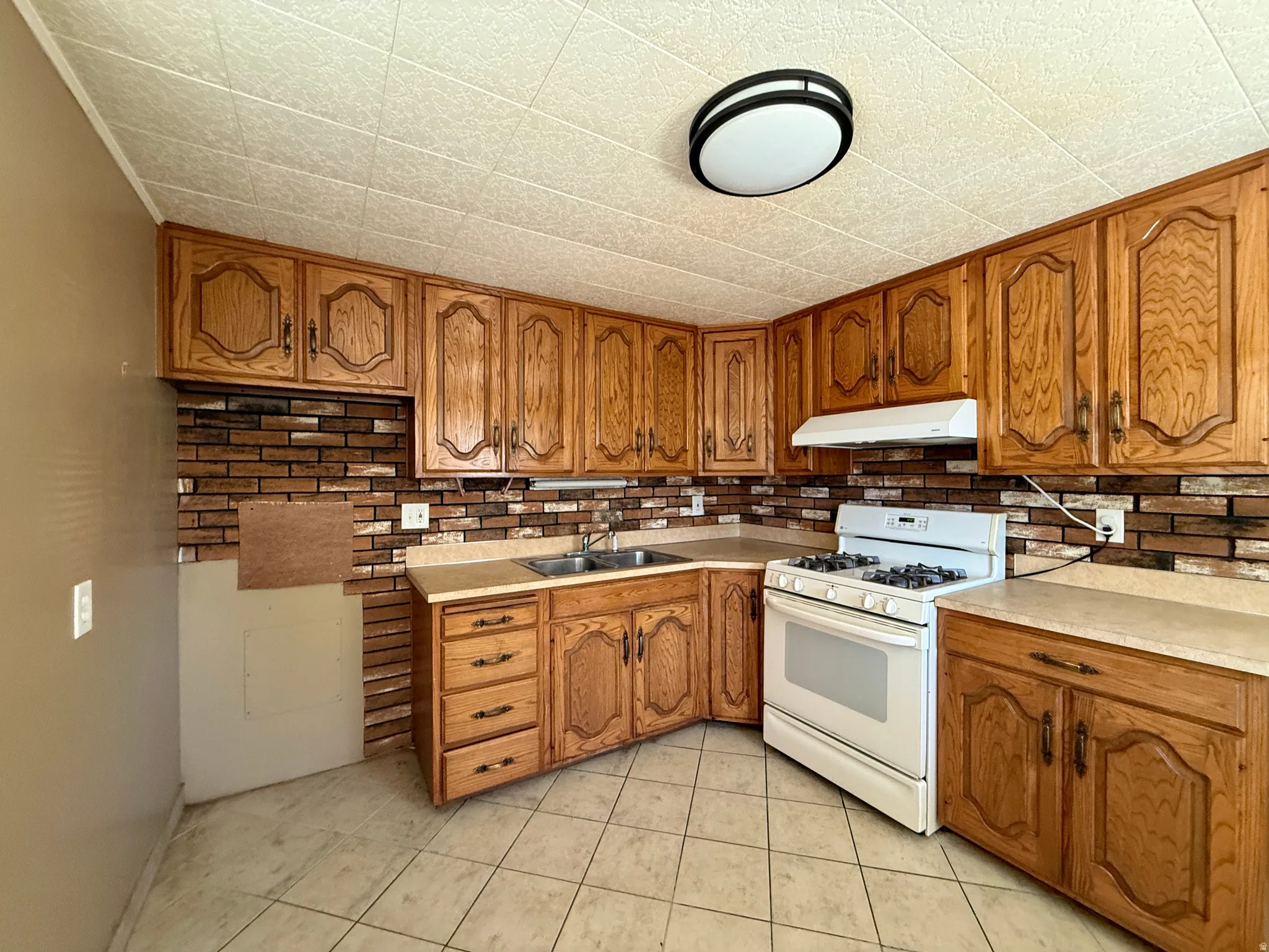 Kitchen featuring wood cabinetry, a gas range with an overhead vent, a stainless steel sink, and a tiled floor
