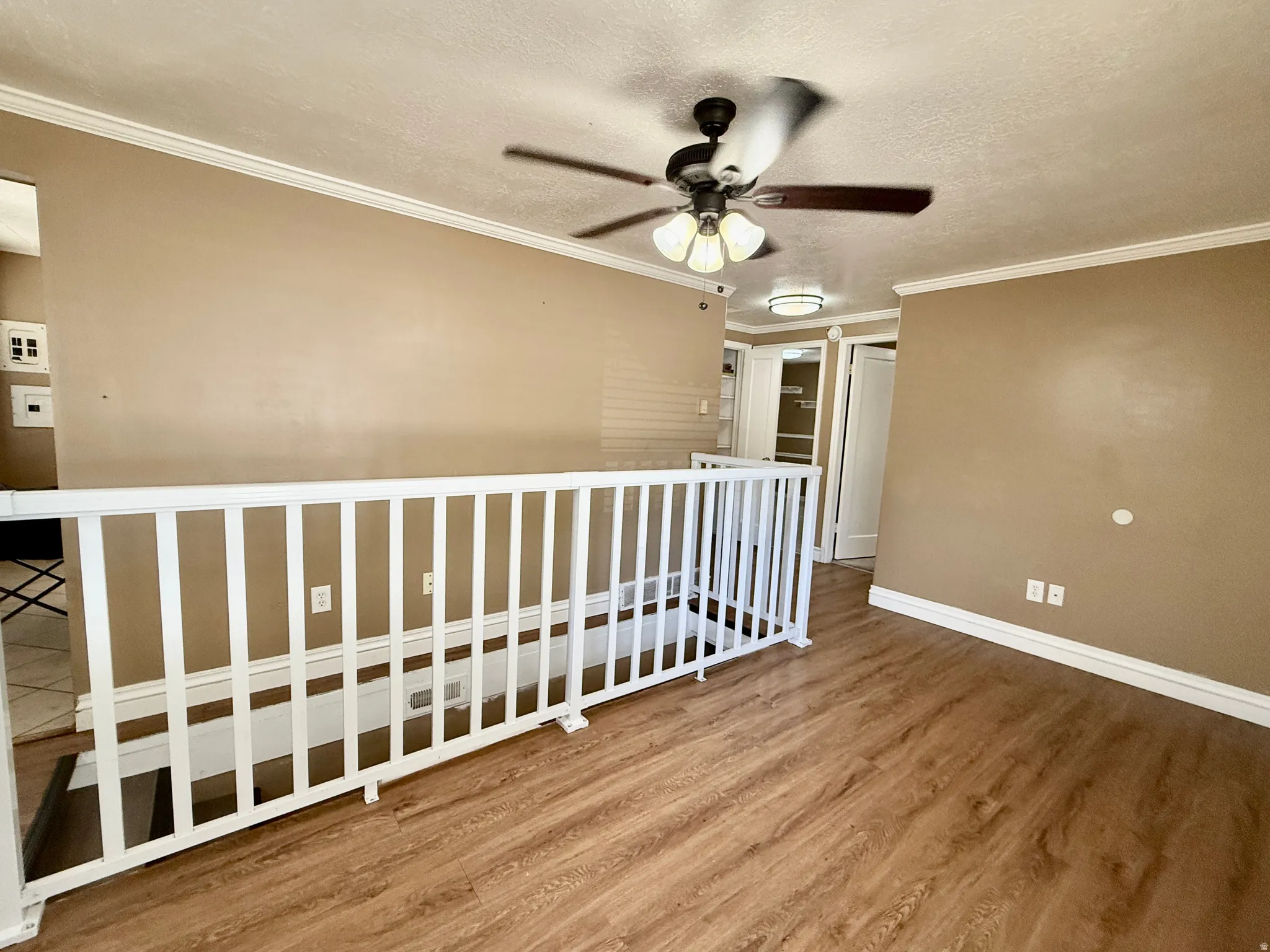 Wood-finish flooring, white railing, crown molding, and ceiling fan with integrated lighting
