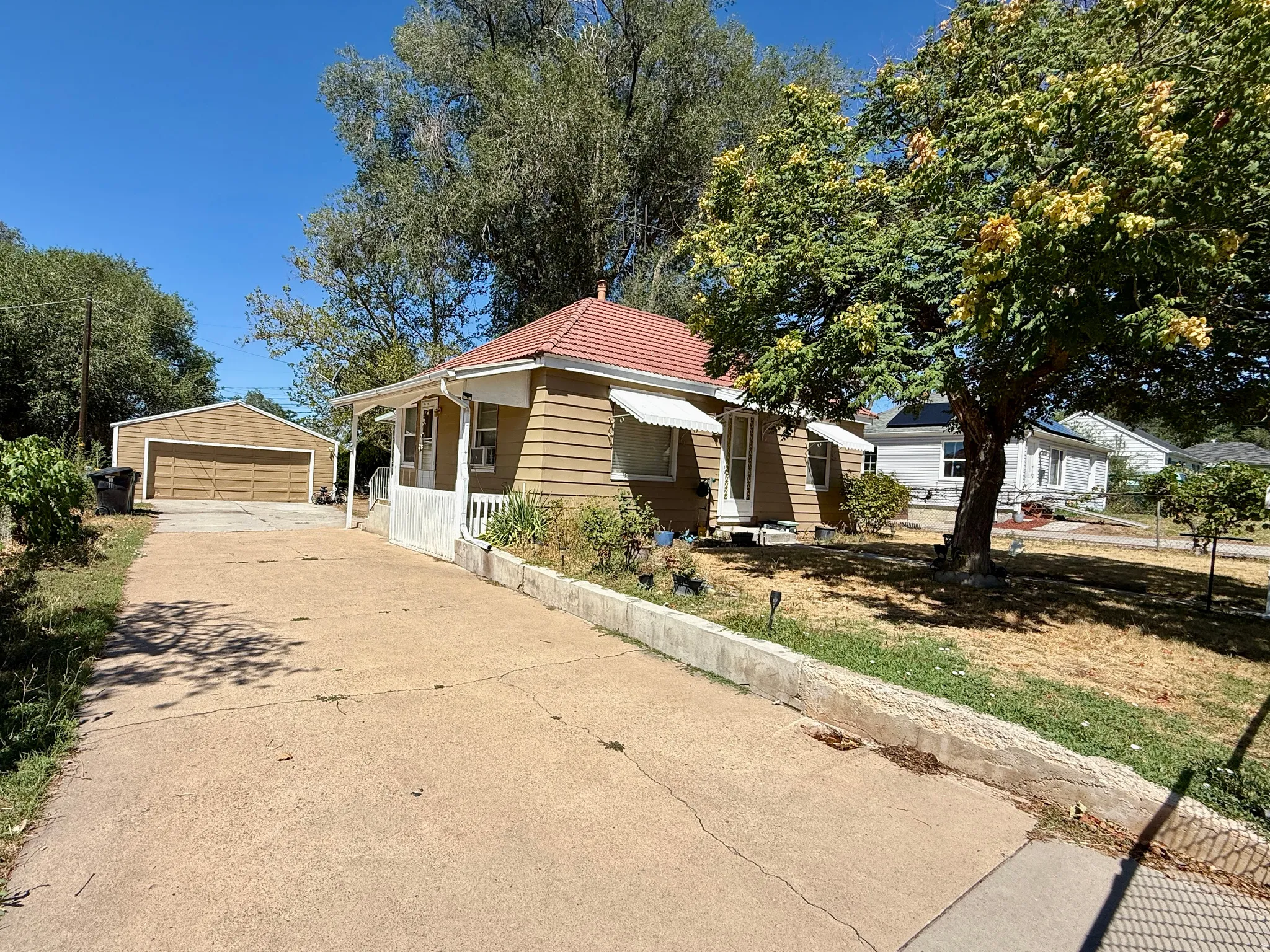 Detached two-car garage, concrete driveway, front porch with railings, and awnings over windows