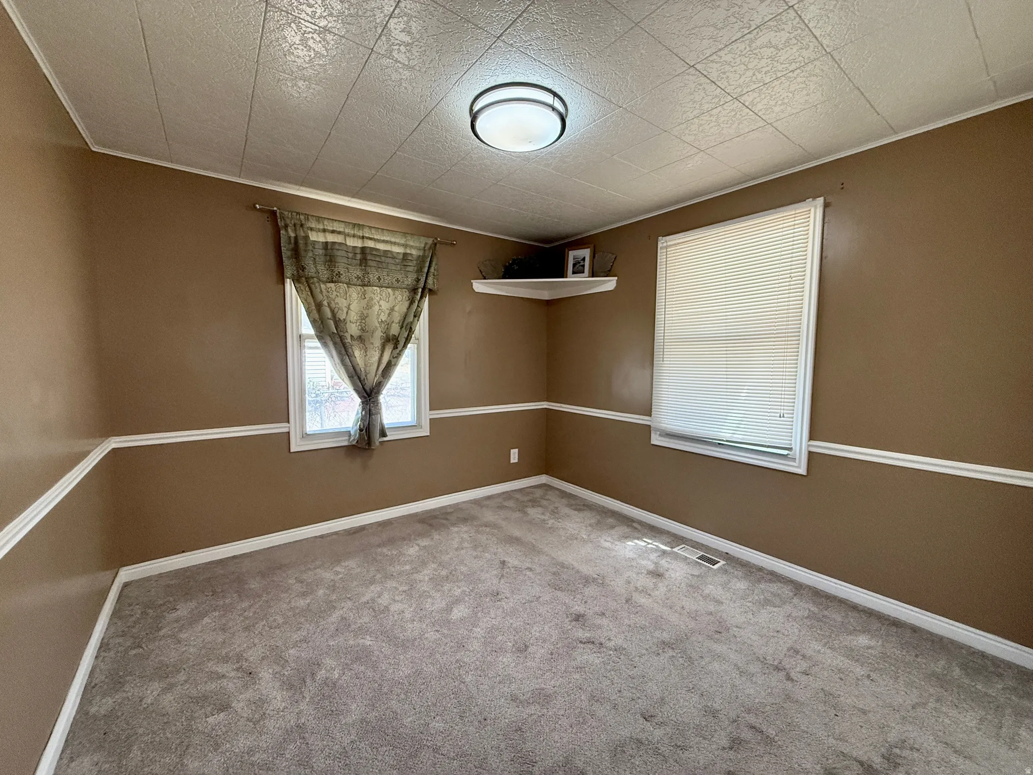 Recessed ceiling light fixture, panel ceiling, two windows, wall molding, and carpeted flooring