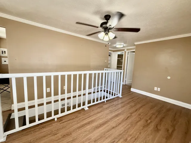 Wood-finish flooring, white railing, crown molding, and ceiling fan with integrated lighting