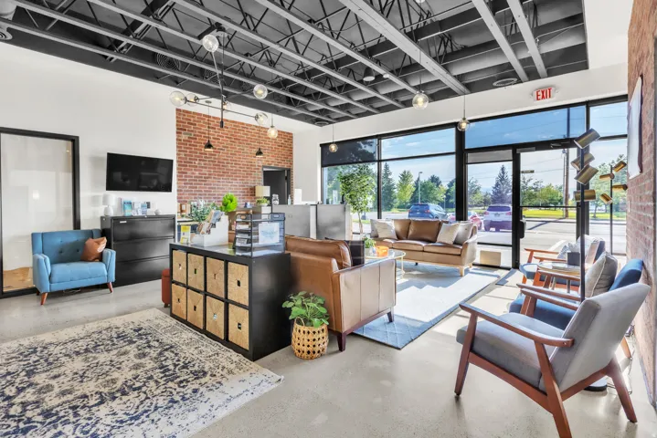 Exposed brick wall accents, industrial-style lighting fixtures, exposed ceiling trusses, large storefront windows, and concrete-finish flooring