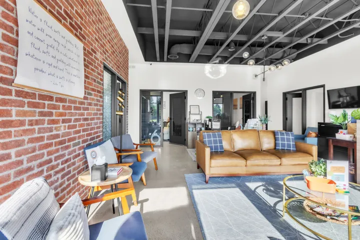 Exposed brick accent wall, concrete flooring, black exposed ceiling beams, multiple modern light fixtures, and black-framed interior doors