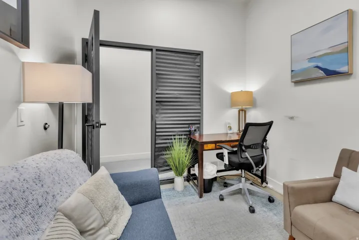 White walls, dark-framed interior door, light-toned area rug, and wood-finish desk