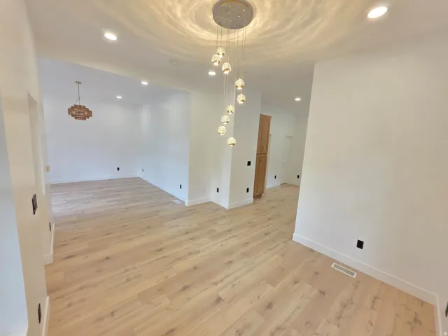 Light wood-finish flooring throughout, recessed ceiling lighting, and a modern chandelier