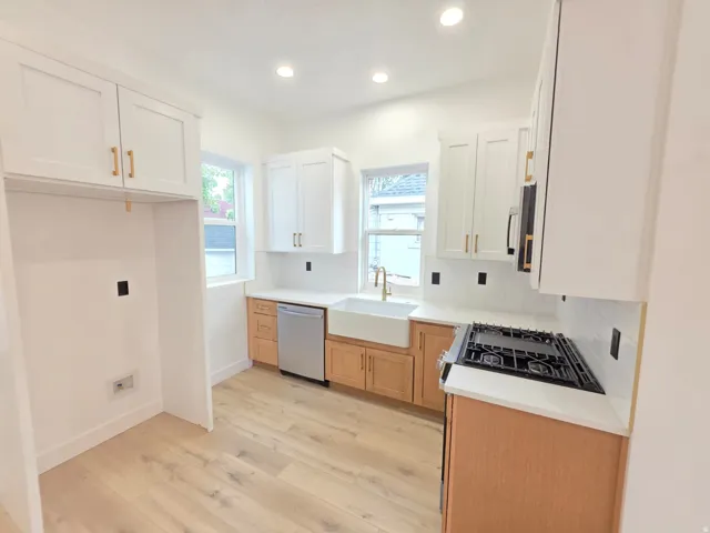 Kitchen featuring wood-finish flooring, white shaker cabinetry, white countertops, a gas range, and a built-in farmhouse sink