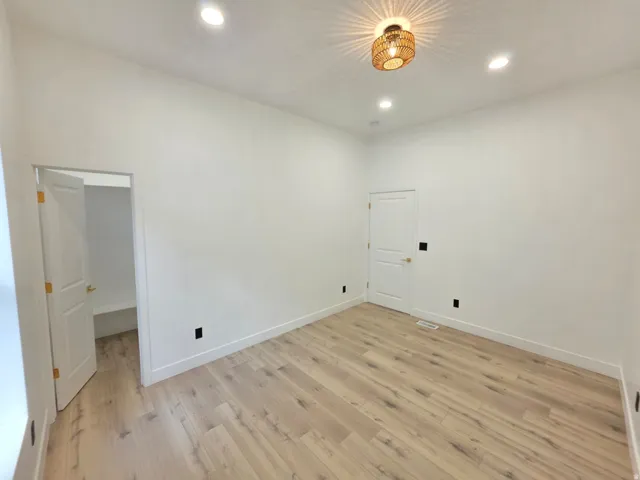 Light wood-finish flooring, recessed ceiling lighting, textured ceiling light fixture, white walls, and white interior doors