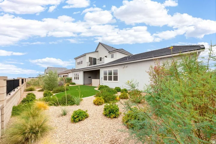 Two-story exterior with a covered patio, second-story balcony, and a low-maintenance yard featuring artificial turf and gravel landscaping