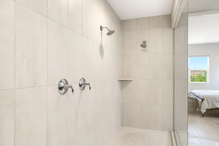 Tiled shower with dual shower heads, chrome fixtures, and a built-in shelf