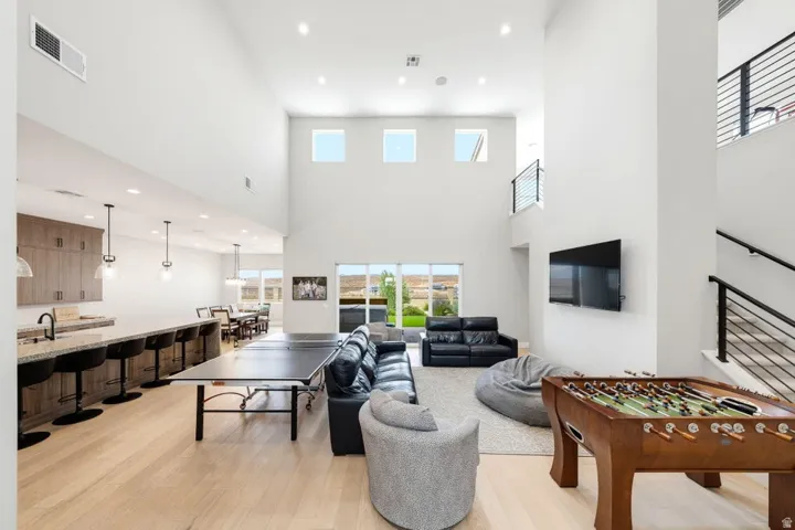 Soaring ceilings with recessed lighting, integrated kitchen island with pendant lighting, wood-finish flooring, staircase with metal railings, and a wall-mounted television