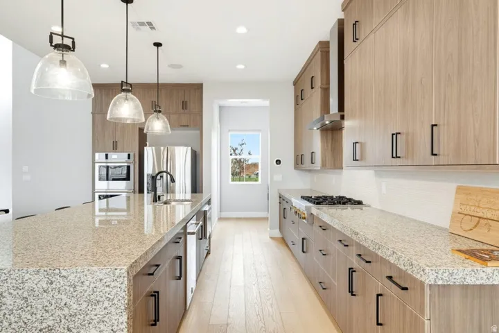 Spacious kitchen featuring light wood-finish cabinetry, granite-pattern countertops, stainless steel appliances, and light wood-finish flooring