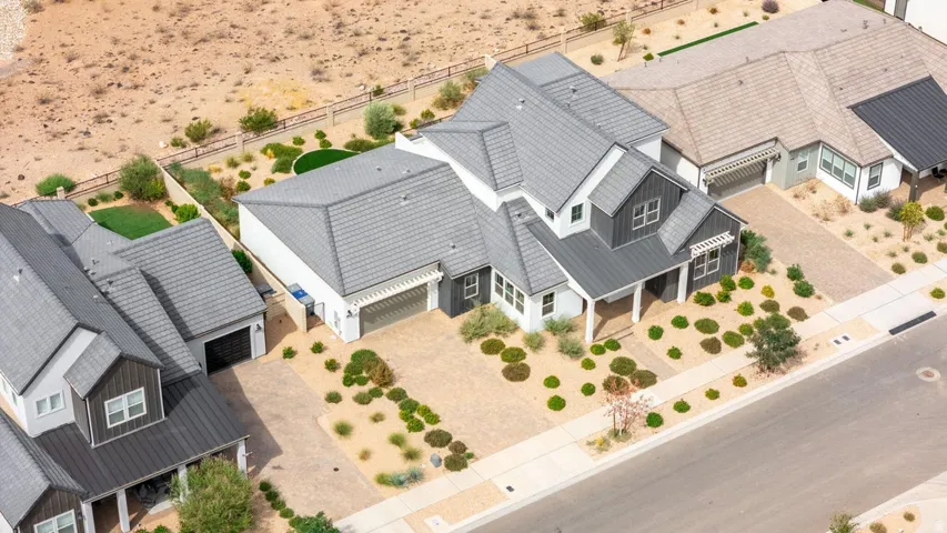 Modern farmhouse architecture with a gray tile roof, covered front porch, and desert-style landscaping