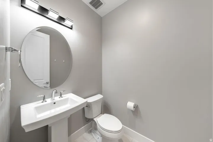 Pedestal sink with chrome faucet, circular mirror, and overhead vanity lighting