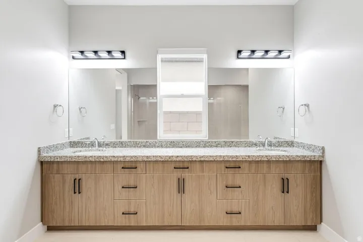 Double vanity with stone-finish countertop, dual integrated sinks, and wood-finish cabinetry featuring matte black hardware