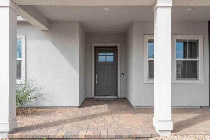 Inviting covered entry with a neutral-toned door, recessed lighting, and a multi-toned paver porch