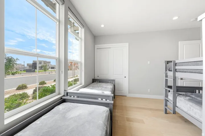 Bright bedroom with expansive windows overlooking neighborhood streetscape, wood-finish flooring throughout, and built-in shelving with multiple storage compartments