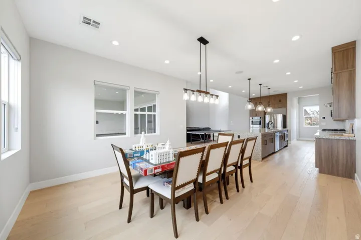 Open-concept living space with light wood-finish flooring, recessed lighting, and a modern linear chandelier