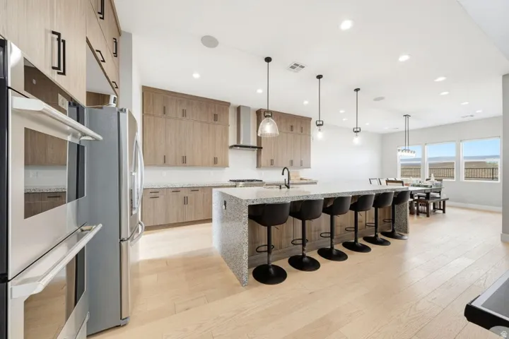 Open-concept kitchen featuring light wood-finish cabinetry, stainless steel appliances, a large center island with counter seating, and light wood-finish flooring
