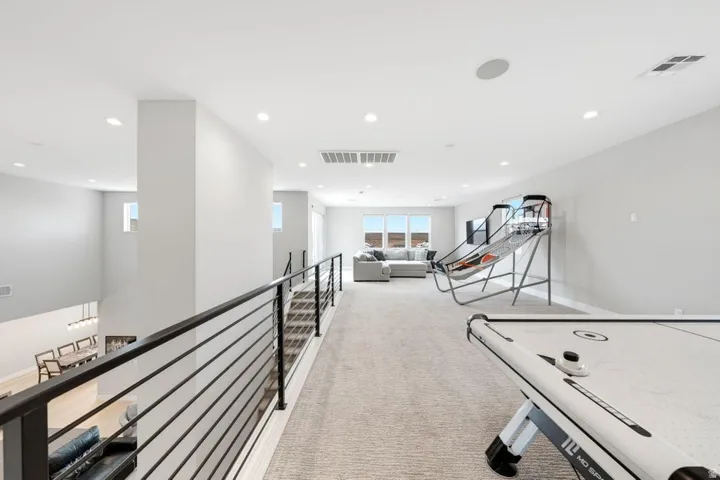 Spacious upper-level landing with carpeted flooring, recessed lighting, and a contemporary black metal railing