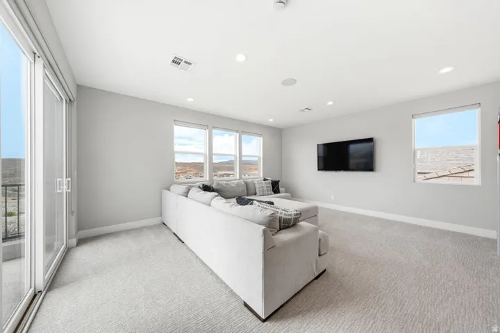 Recessed lighting, light-toned carpeting, multiple windows, and a sliding glass door with a balcony