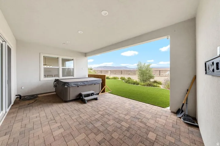 Covered patio with paver flooring, built-in spa, artificial turf lawn, and distant mountain scenery