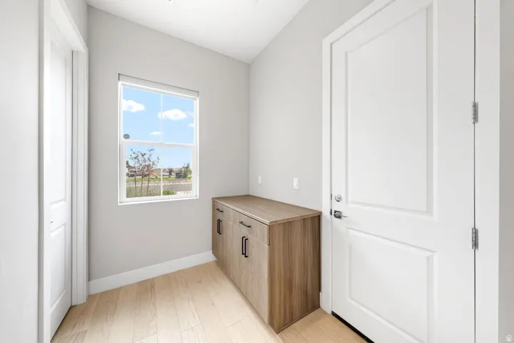 Wood-finish flooring, built-in cabinetry with dark pulls, light gray walls, and a white framed window