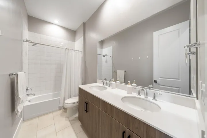 Dual vanity with undermount sinks and wood-finish cabinetry, white countertop, large wall-mounted mirror, and a shower-over-tub with white subway tile surround