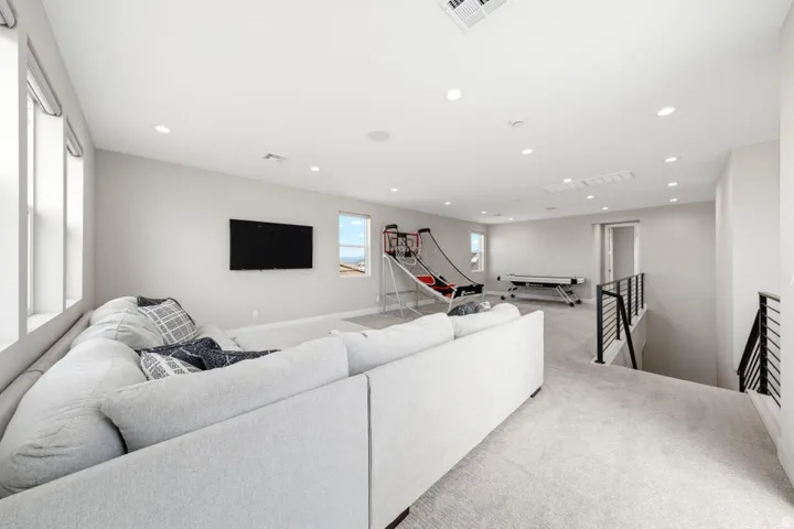 Carpeted room with multiple windows, recessed lighting, and a black metal railing