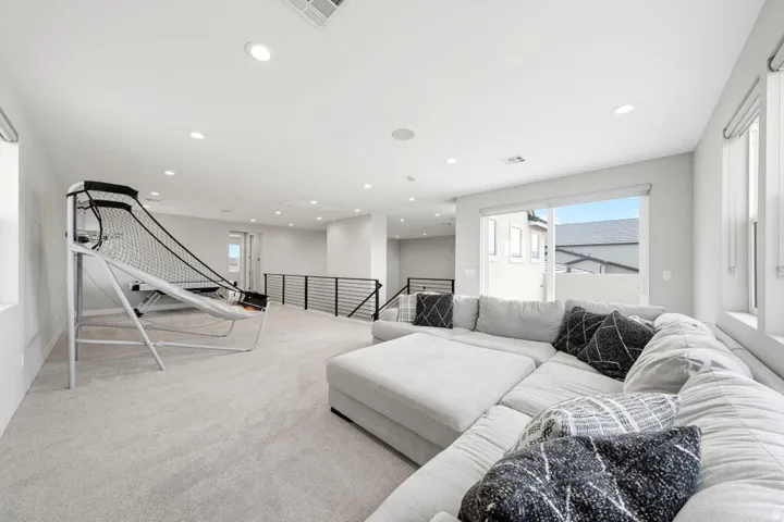 Expansive open space with light-toned carpeting, recessed ceiling lighting, and a black metal railing