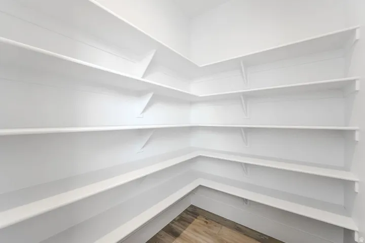 Corner pantry with extensive white shelving and wood-finish flooring