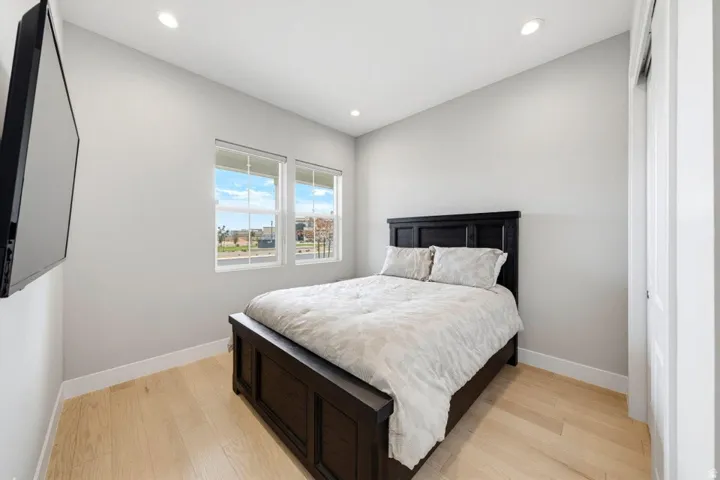 Bright secondary bedroom showcasing a wood-finish plank floor, black wood bed frame, and large dual-pane windows flooding the space with natural light