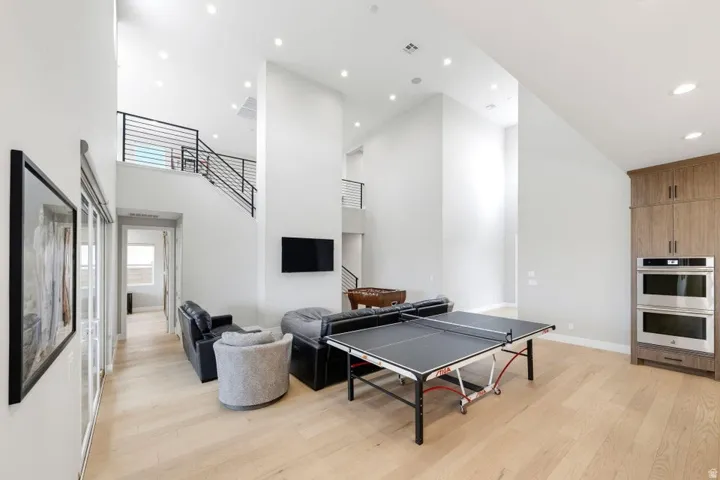 Spacious interior with light wood-finish flooring, high ceilings, recessed lighting, and a built-in cabinetry unit featuring double ovens