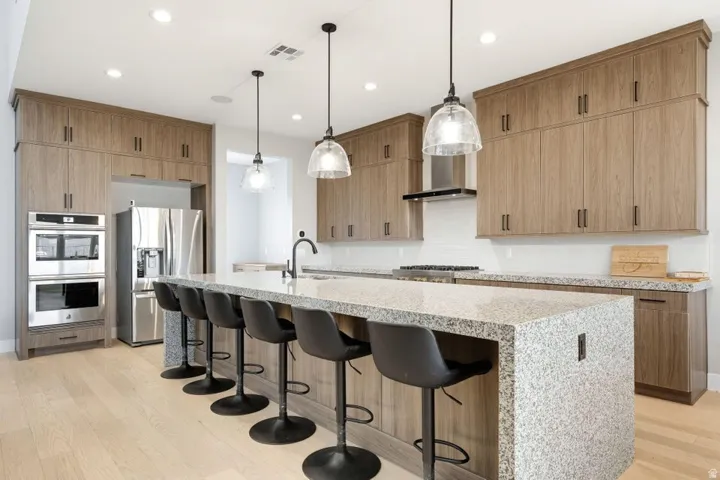 Modern kitchen featuring wood-finish cabinetry, light-toned wood-finish flooring, and a large island with a light-colored countertop