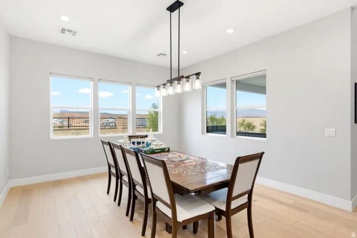 Light wood-finish flooring with recessed lighting and a modern linear chandelier
