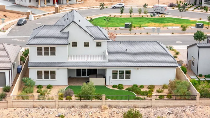 Stucco exterior with a tiled roof, second-story balcony with metal railing, and a fenced backyard featuring artificial turf and desert landscaping