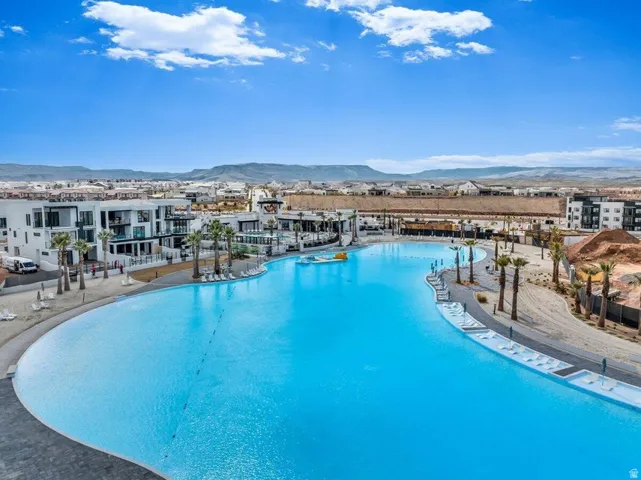 Expansive lagoon featuring clear blue water, adjacent to modern multi-story buildings with balconies, and surrounded by mature palm trees and sandy areas