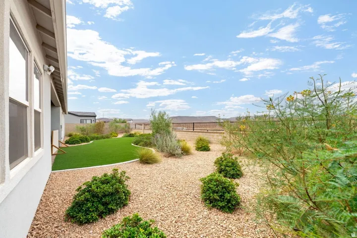 Expansive backyard with mature landscaping, featuring a lush green lawn, decorative shrub plantings, and natural xeriscaping with gravel hardscaping