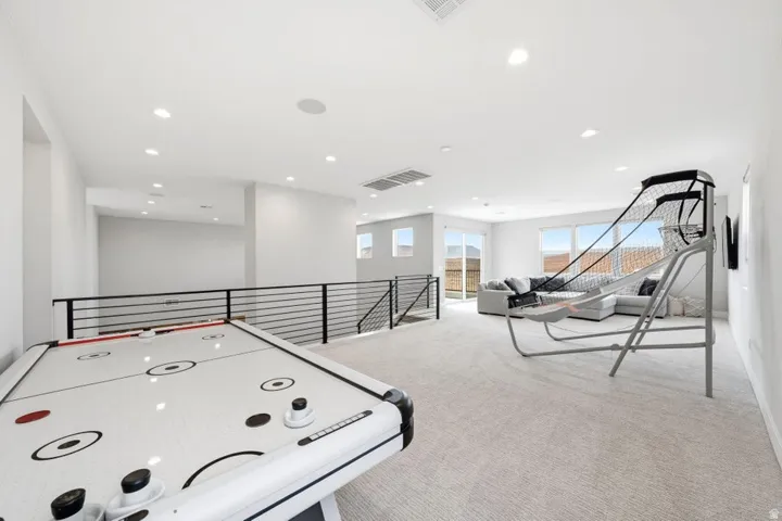 Carpeted upper level with recessed lighting, modern horizontal railing, and multiple windows providing natural illumination