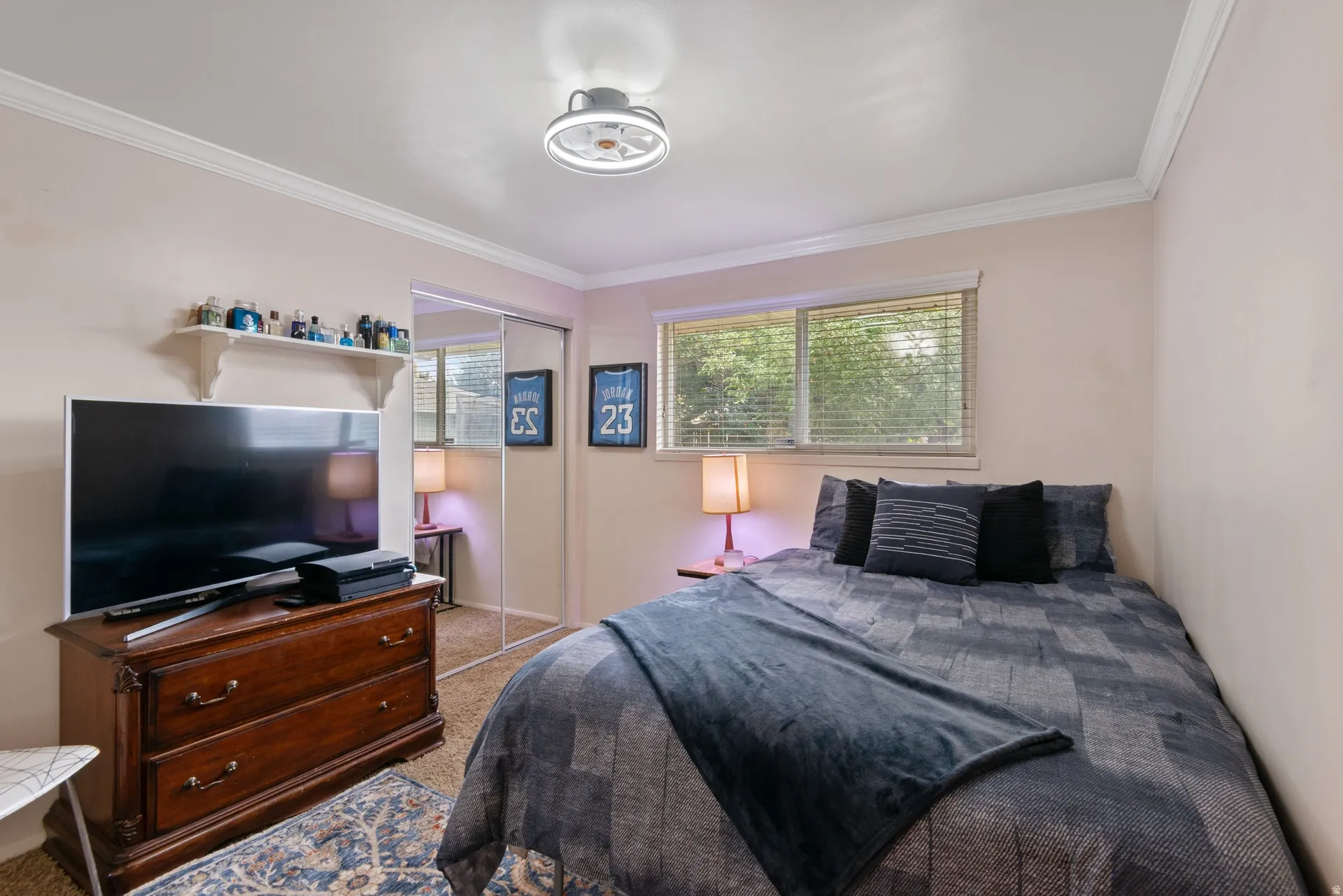 Crown molding, a flush-mount ceiling light with fan, a window with blinds, and mirrored sliding closet doors