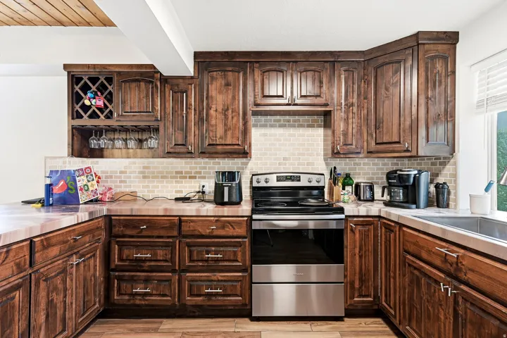 Warm wood cabinetry with detailed paneling and hardware accents frames this kitchen, featuring stainless steel appliances, subway tile backsplash, and a wine rack insert