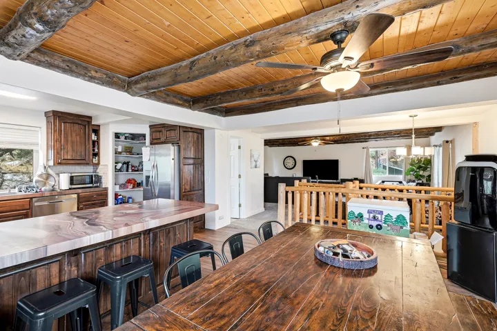 Wood-paneled ceiling with exposed wood beams, wood-finish flooring, dark wood cabinetry, stainless steel appliances, and a kitchen island with a stone-finish countertop