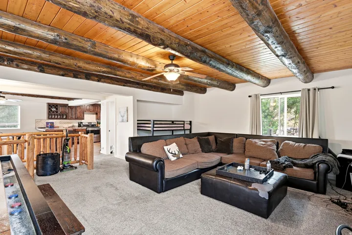 Exposed wood beam ceiling with wood paneling, ceiling fan with light fixture, light gray carpet, and a large window