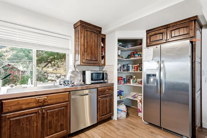 Wood-finish flooring, stainless steel appliances, and wood cabinetry with a tile backsplash