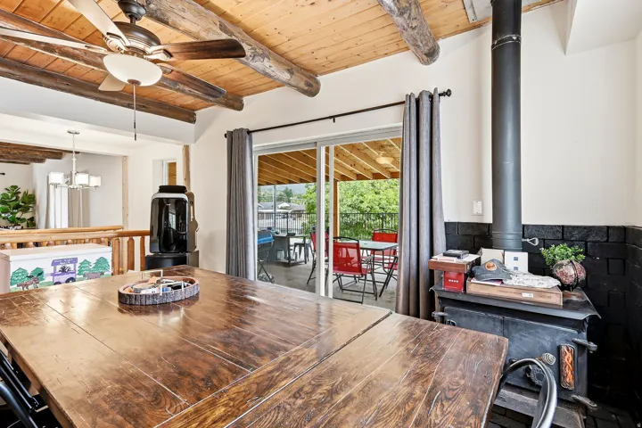 Wood ceiling with exposed beams, ceiling fan, wood-finish flooring, sliding glass door, and a built-in wood-burning stove with a brick surround