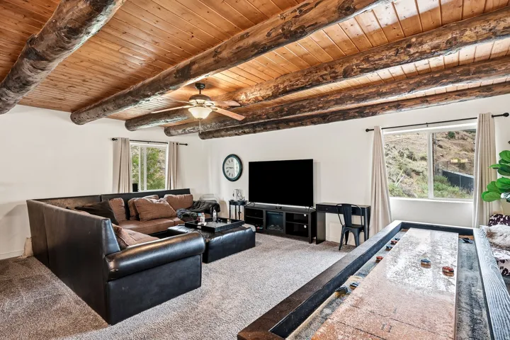 Exposed wood beam ceiling with natural wood plank details, ceiling fan, carpeted flooring, and natural light from multiple windows