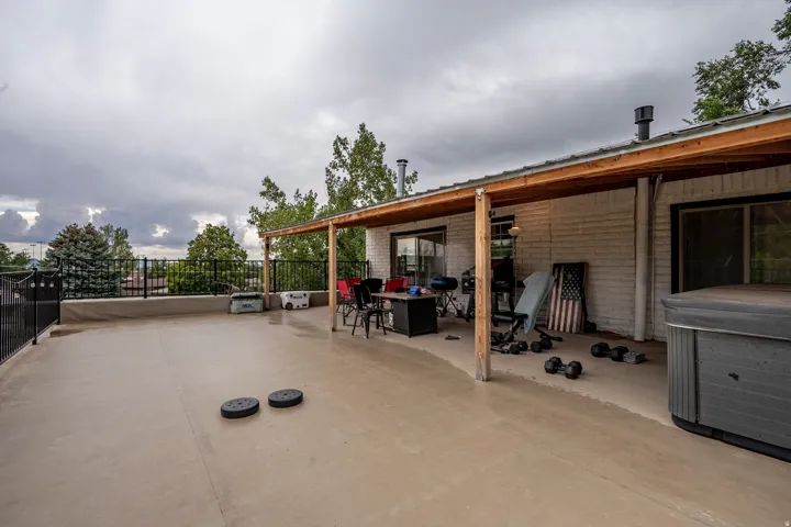 Expansive outdoor patio with a partial wood-framed overhang, white brick exterior, black metal railing, and concrete flooring
